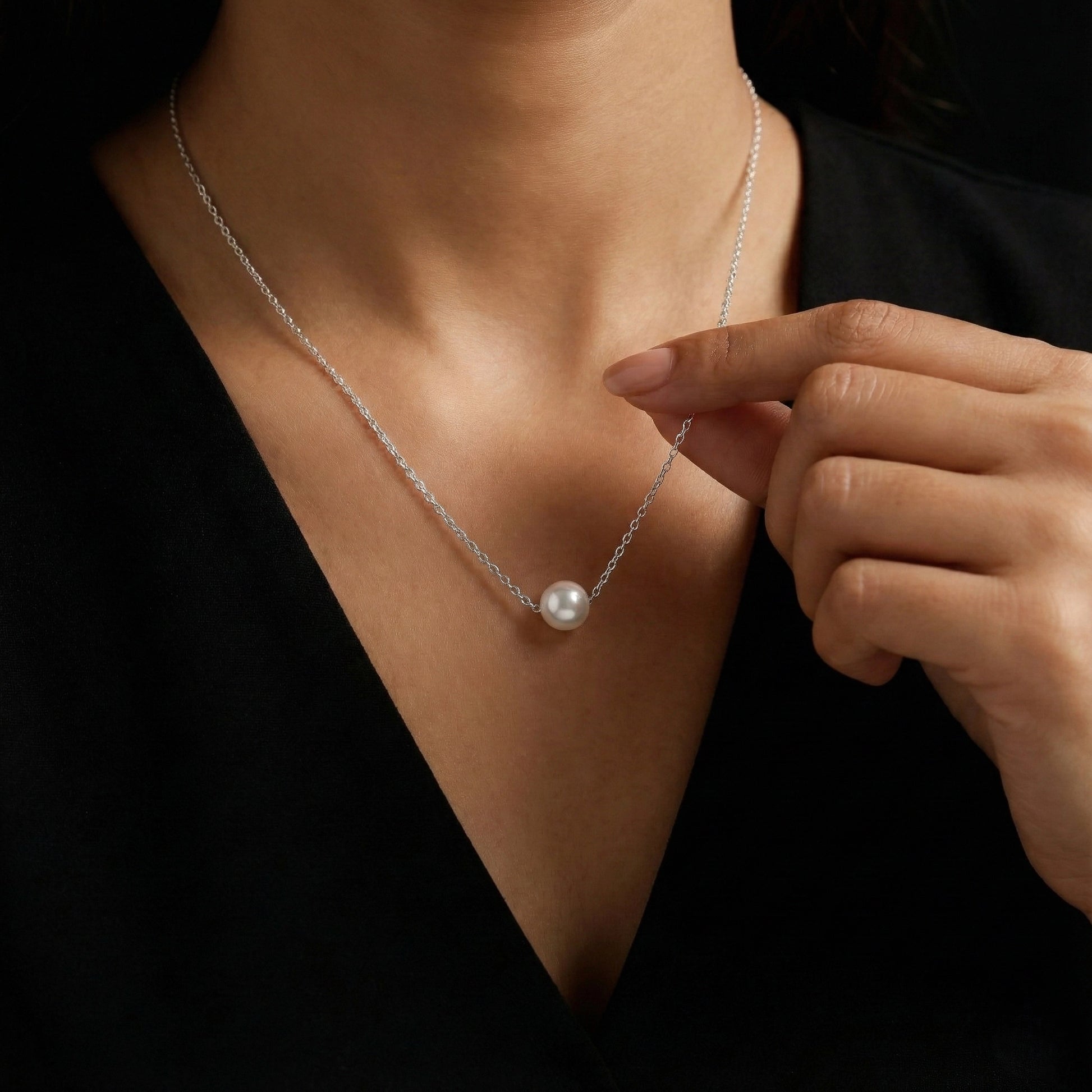 Person wearing a pearl necklace with a hand adjusting it against a dark background
