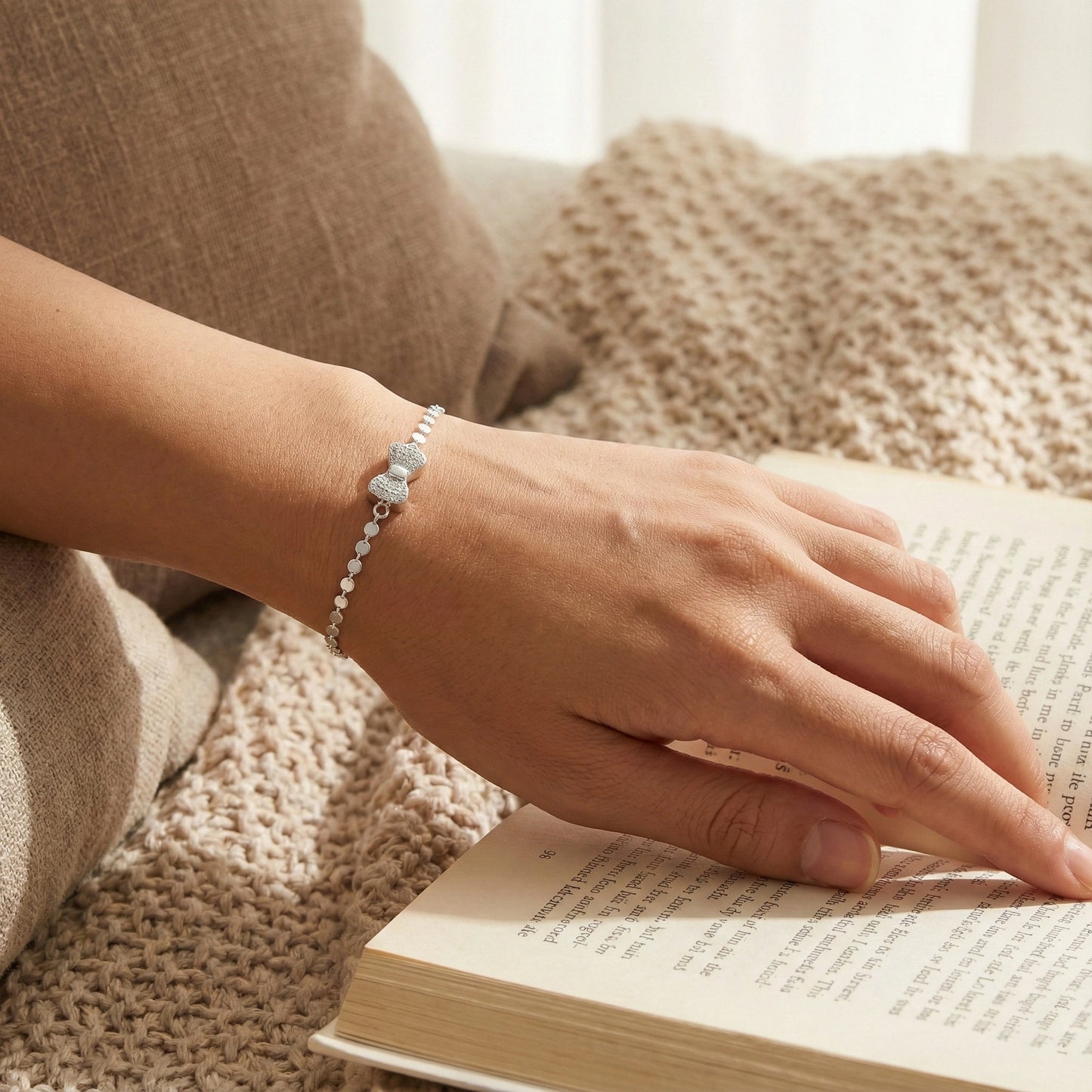 Hand wearing a bracelet on an open book with a soft, warm background