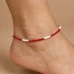 Red beaded anklet on a person's ankle against a beige background
