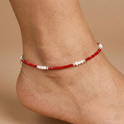 Red beaded anklet on a person's ankle against a beige background