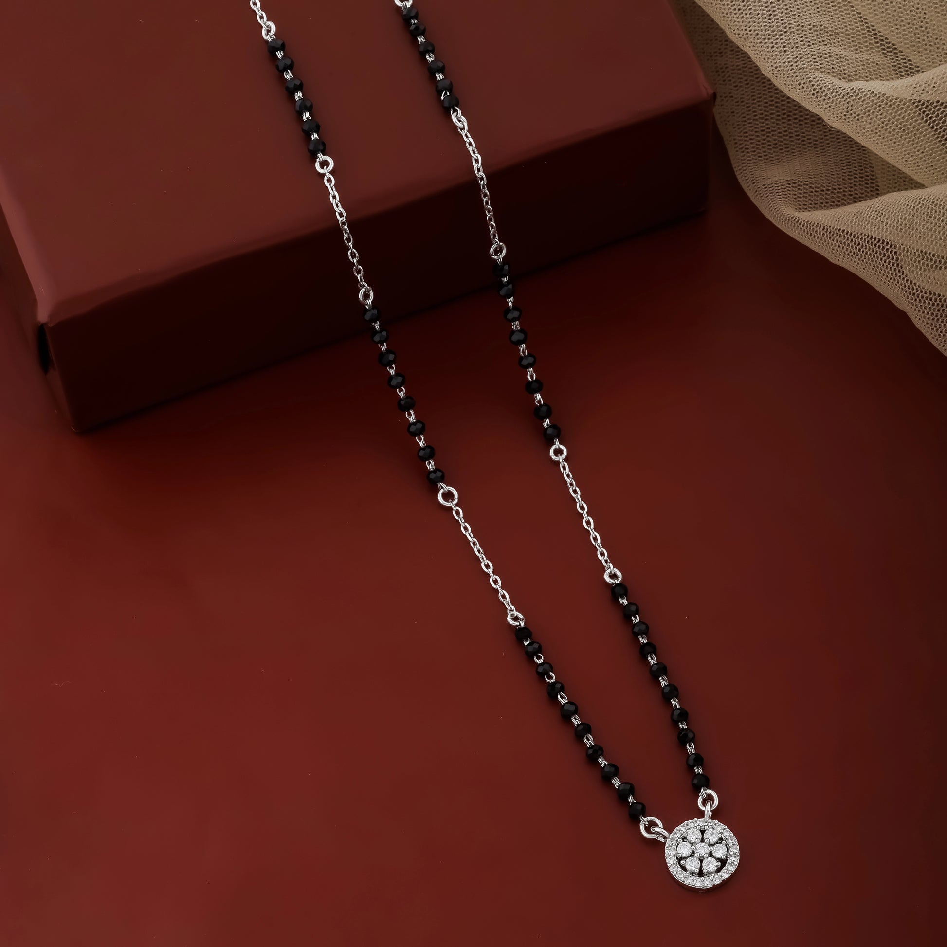Necklace with black beads and a silver pendant on a brown surface
