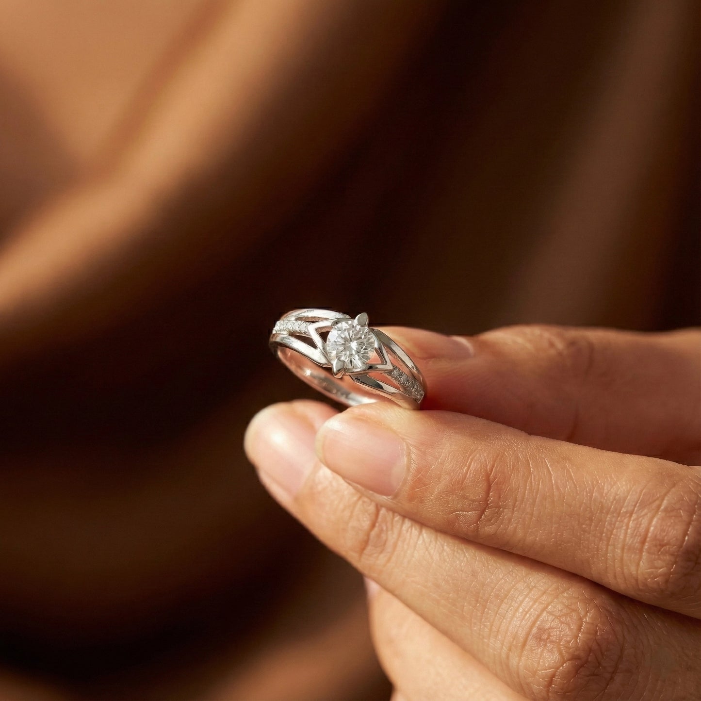 Silver ring with a diamond held between fingers against a blurred brown background
