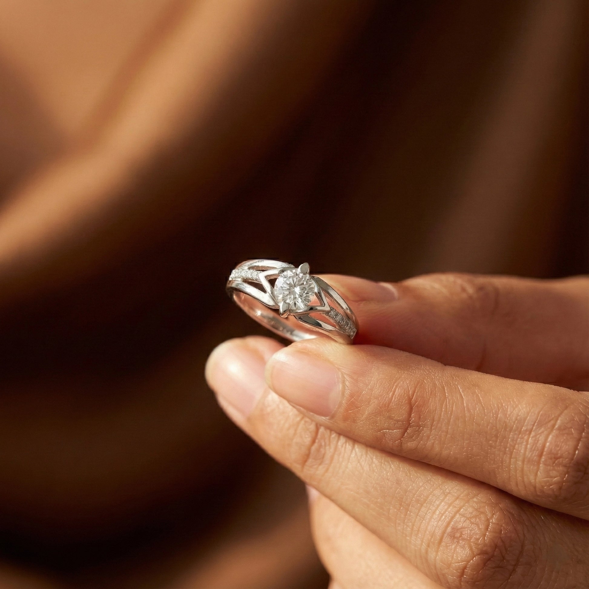 Silver ring with a diamond held between fingers against a blurred brown background