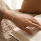 Hand wearing a silver bracelet on an open book with a blurred background