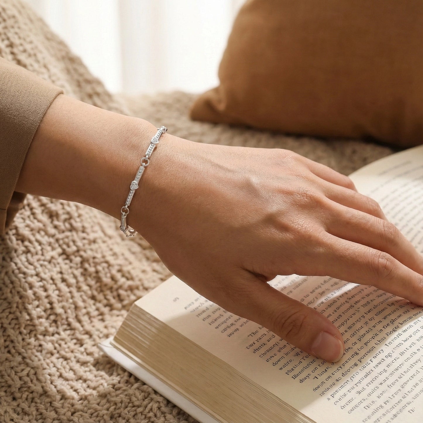 Hand wearing a silver bracelet on an open book with a blurred background