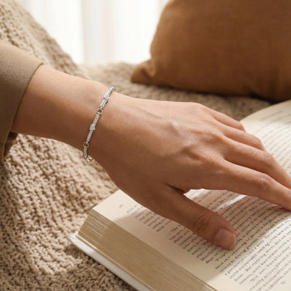 Hand wearing a silver bracelet on an open book with a blurred background