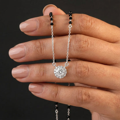 Hand holding a silver necklace with a round pendant against a dark background