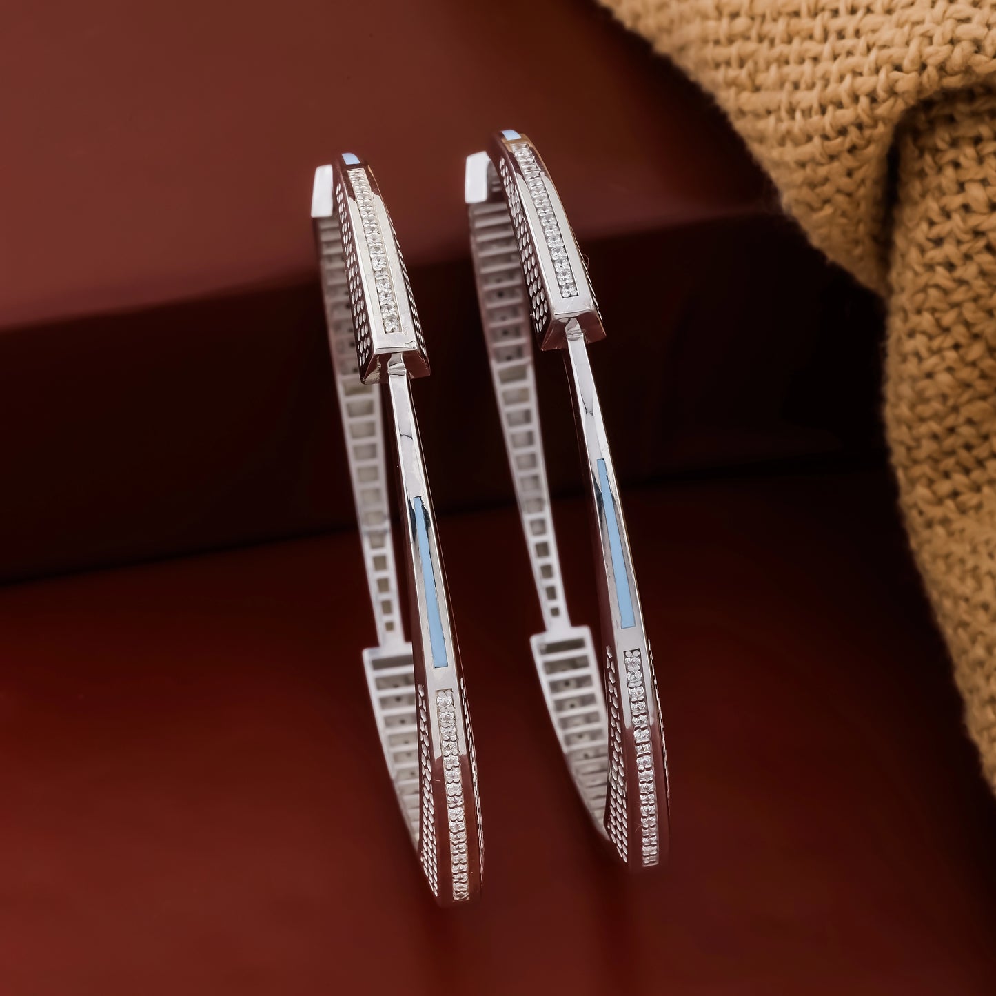 Pair of silver hoop earrings with embedded stones on a brown textured background