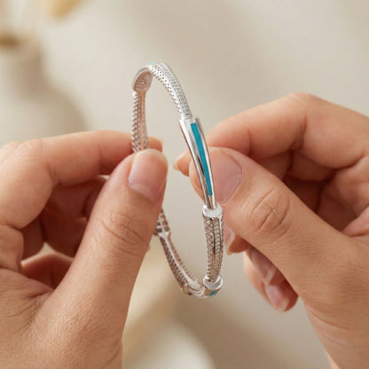 Close-up of hands holding a silver bracelet with a blue accent against a neutral background