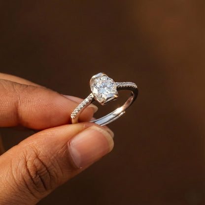Silver ring with a large diamond held by a hand against a brown background