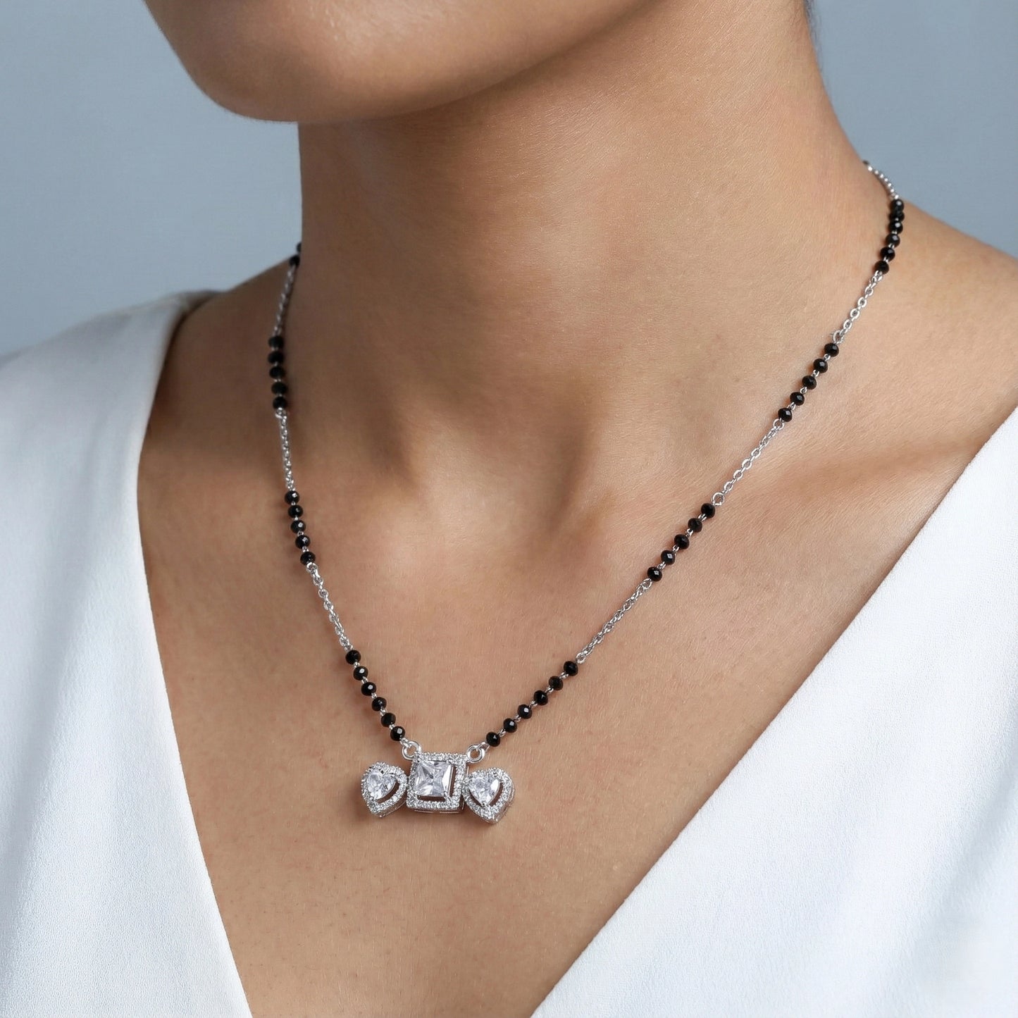Necklace with black beads and silver pendant on a person wearing a white top.