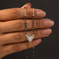 Hand holding a necklace with a black beaded chain and silver clasp against a dark background