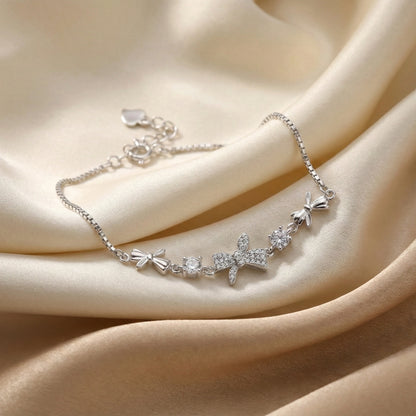 Silver bracelet with floral and bow designs on a beige fabric background