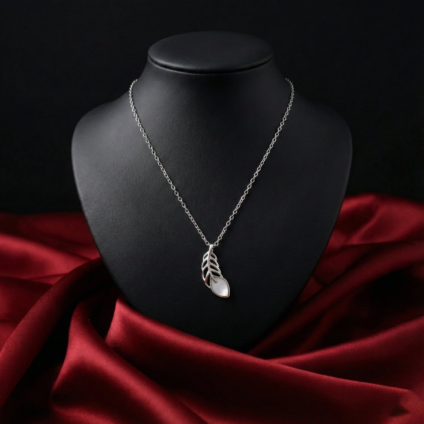 Silver necklace with a leaf pendant on a black mannequin bust against a red fabric background