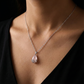 Necklace with a pink teardrop pendant on a person wearing a black top.