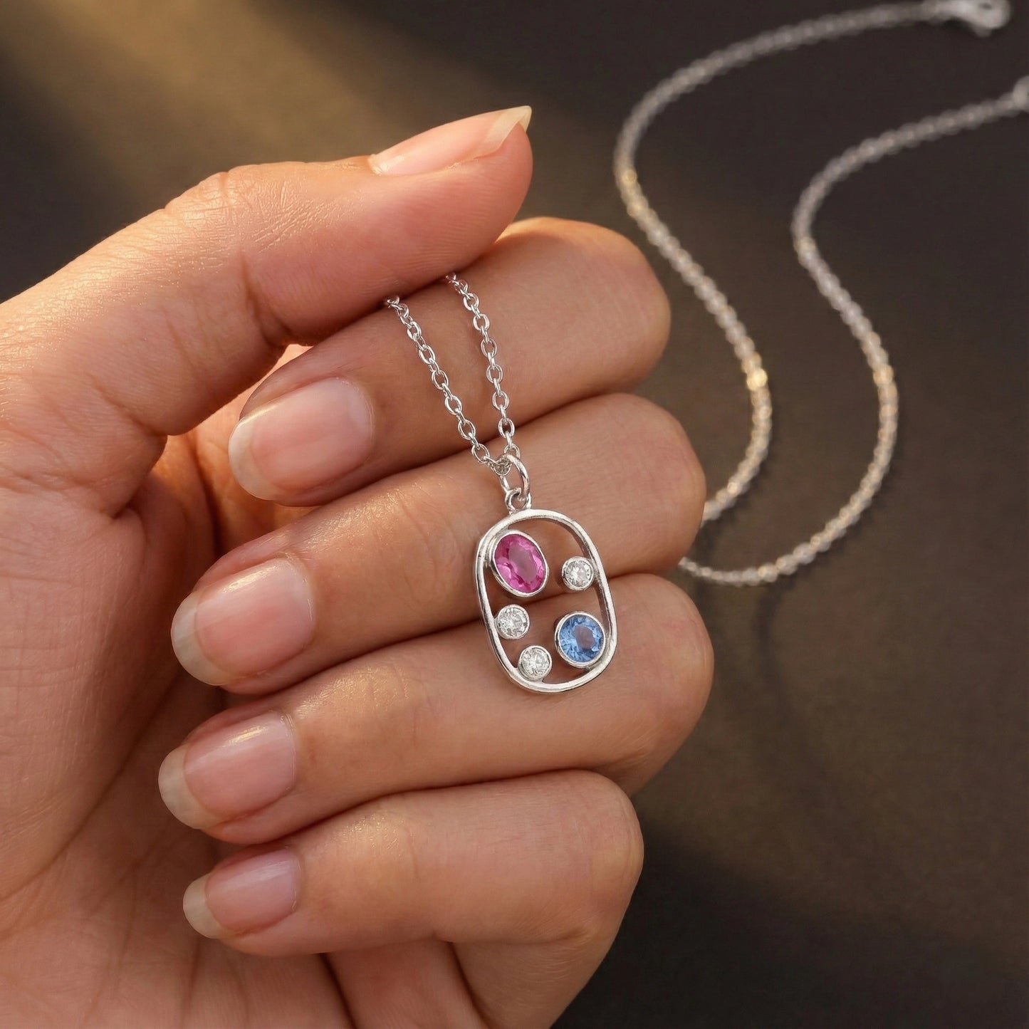 Hand holding a silver necklace with a colorful pendant against a blurred background