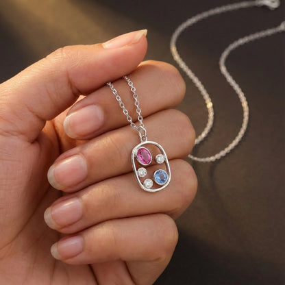 Hand holding a silver necklace with a colorful pendant against a blurred background