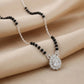 Necklace with black beads and a silver pendant on a beige fabric background