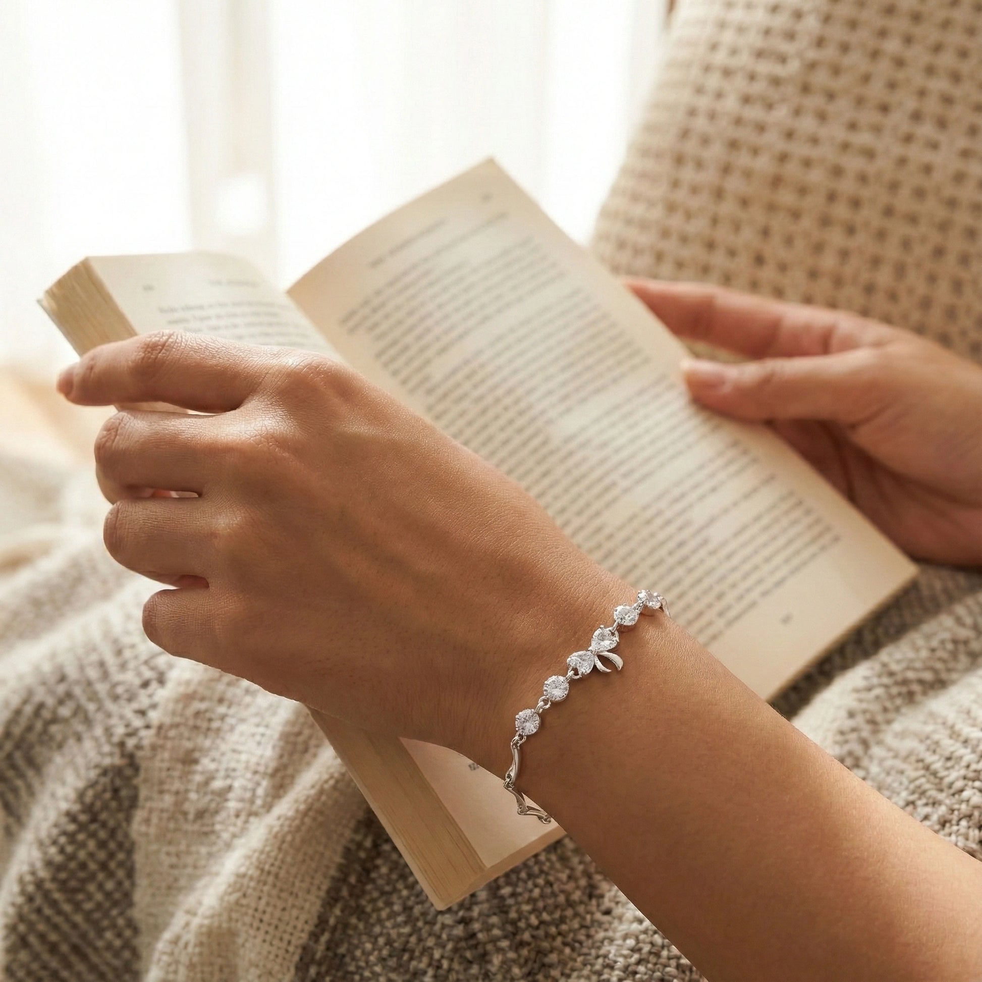 Person reading a book with a bracelet on wrist, sitting in a cozy setting.