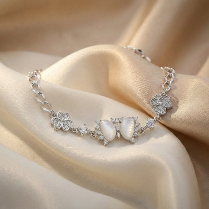 Silver bracelet with floral and shell designs on a beige fabric background