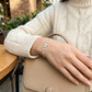 Person wearing a silver bracelet with a beige sweater and handbag in an outdoor setting