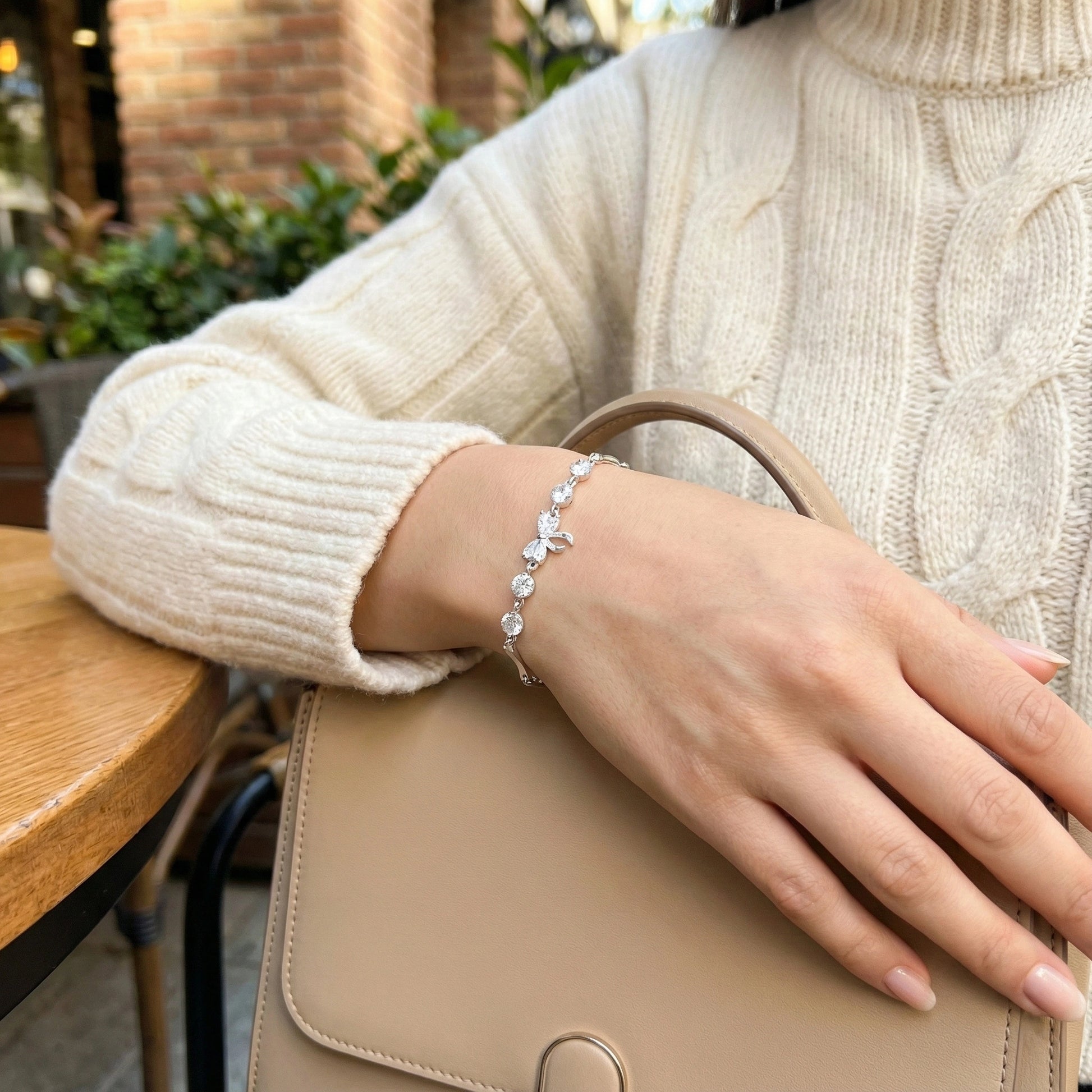 Person wearing a silver bracelet with a beige sweater and handbag in an outdoor setting