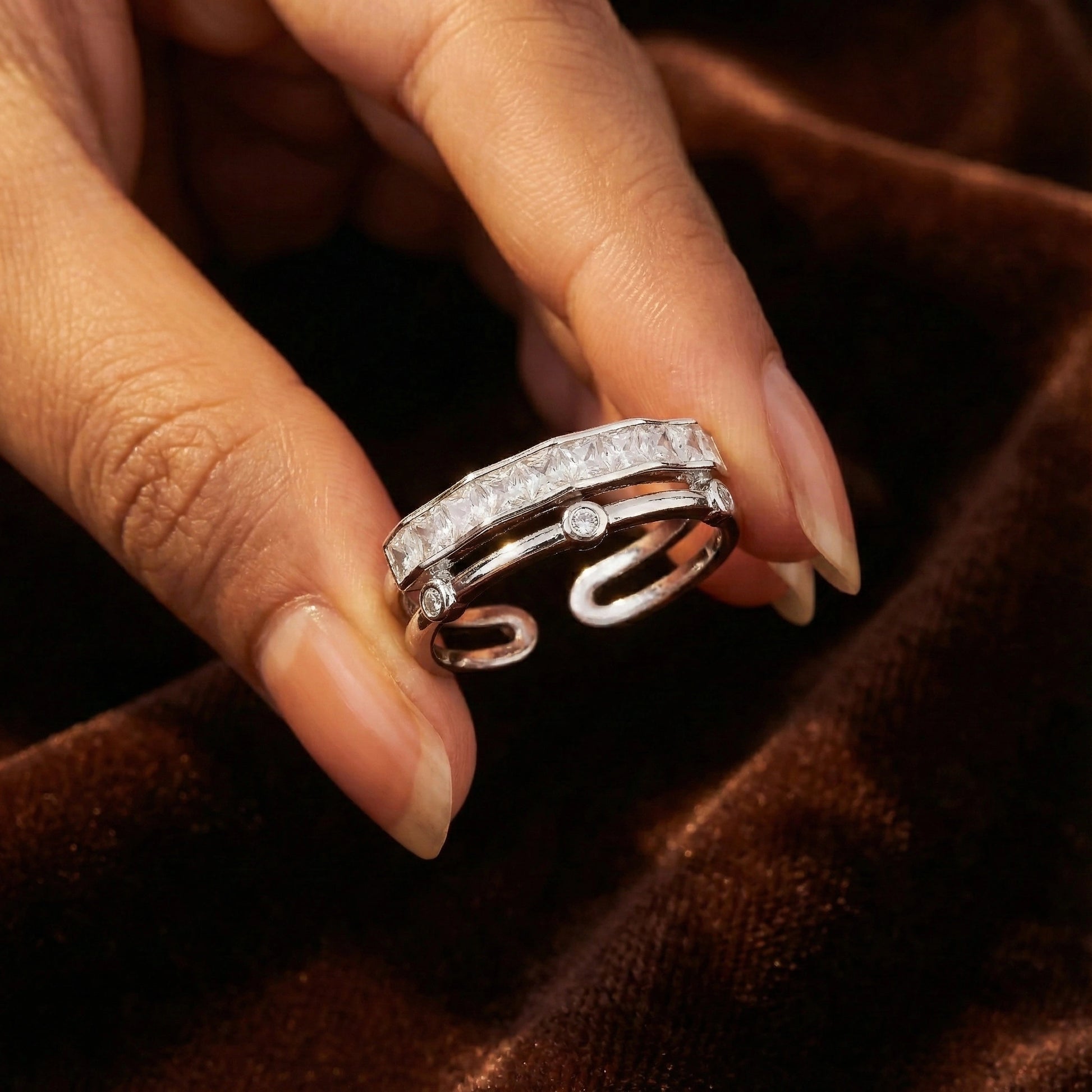 Silver ring with diamonds held between fingers on a brown fabric background