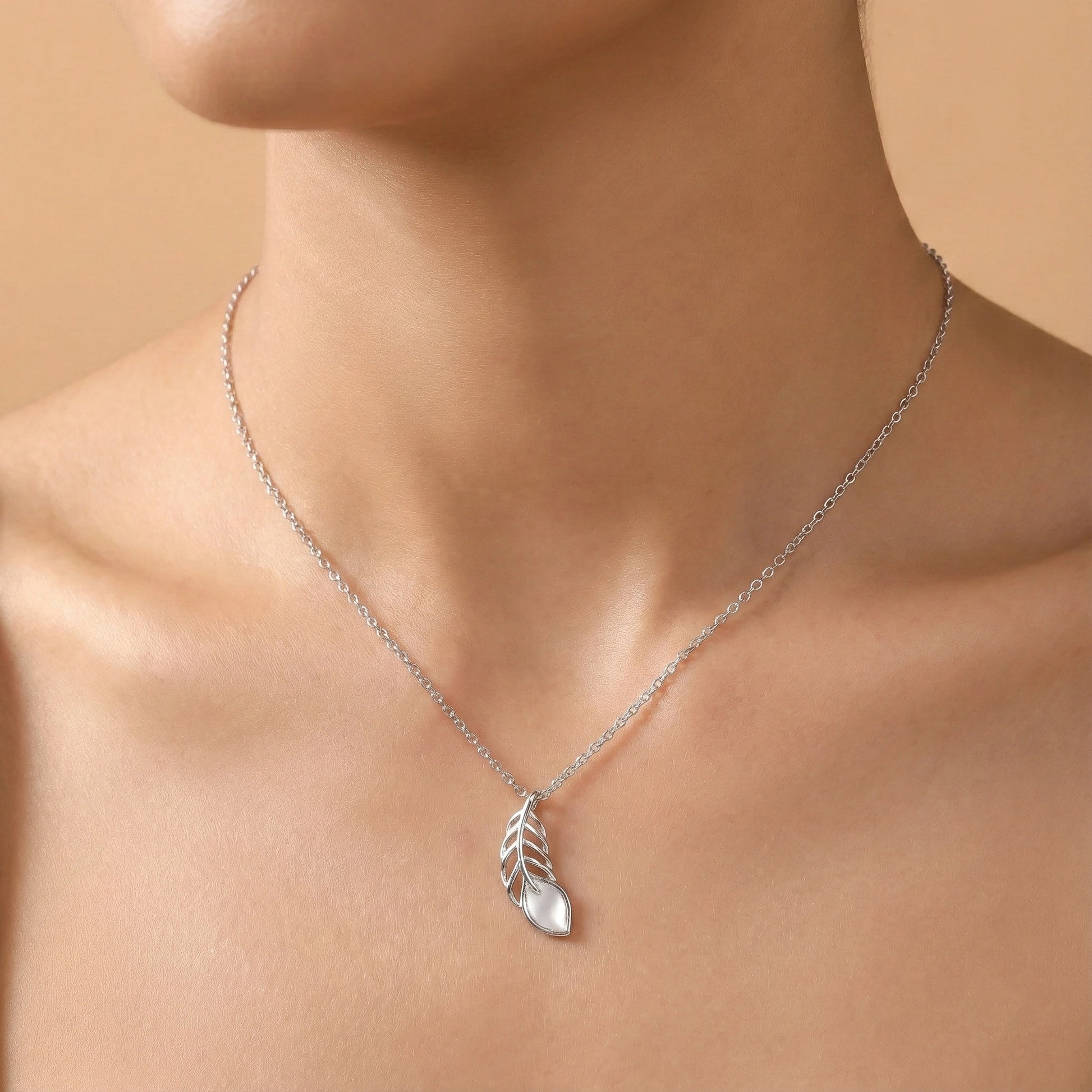 Silver necklace with a leaf pendant on a person's neck against a beige background