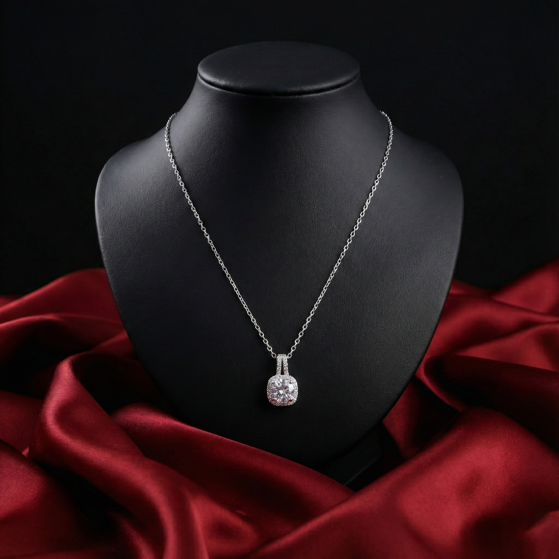Silver necklace with a pendant on a black mannequin bust against a red fabric background