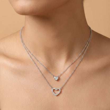 Silver necklaces with heart and round pendants on a person's neck against a beige background