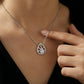 Teardrop-shaped diamond necklace on a person's neck with a hand pointing to it.