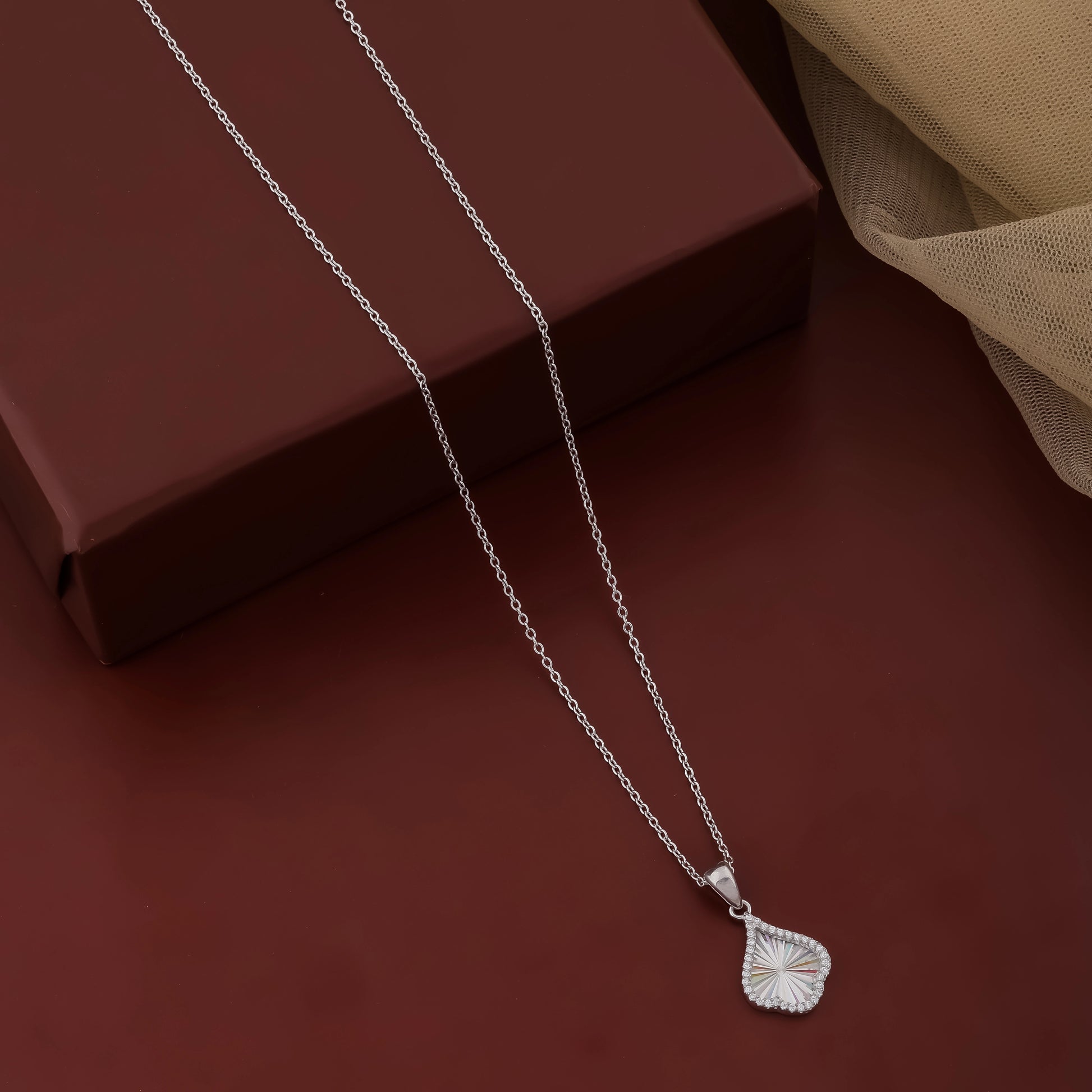 Silver necklace with a leaf pendant on a dark red surface