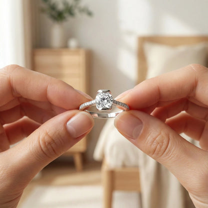 Close-up of a diamond ring held between two hands with a blurred indoor background
