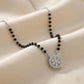 Necklace with black beads and a silver pendant on a beige fabric background