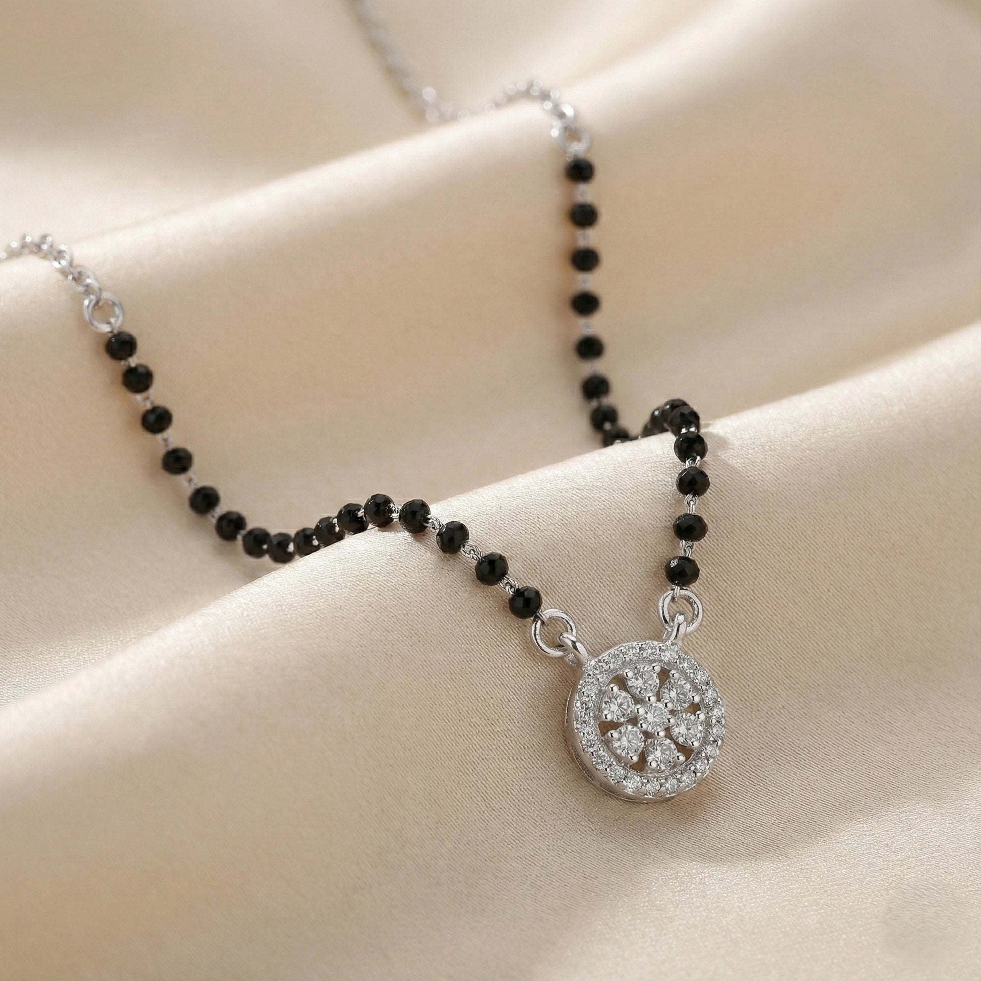 Necklace with black beads and a silver pendant on a beige fabric background