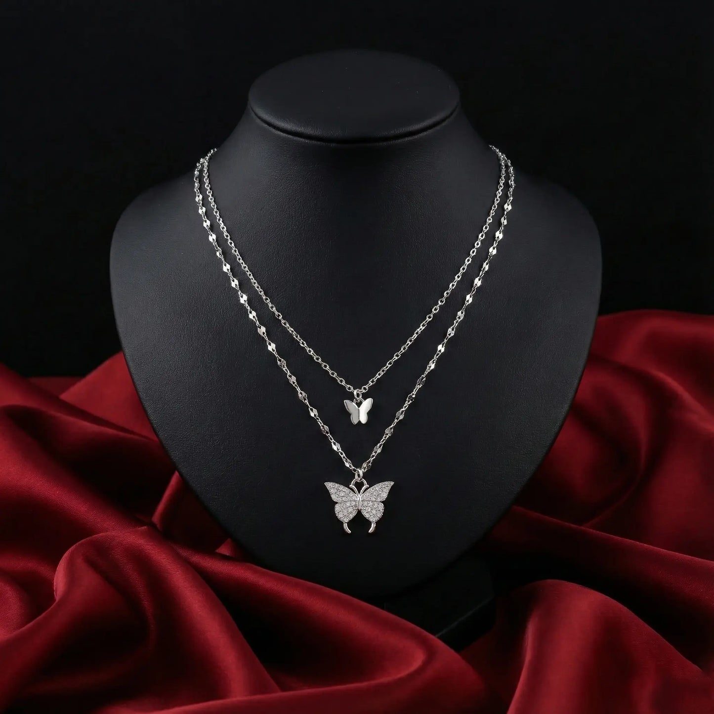 Silver butterfly necklace on a black mannequin bust with a red fabric background