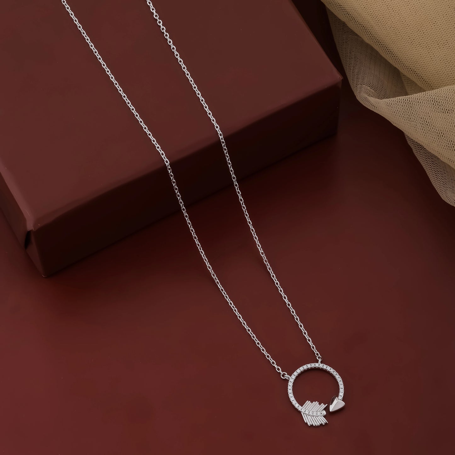 Silver necklace with a circular pendant on a dark red surface