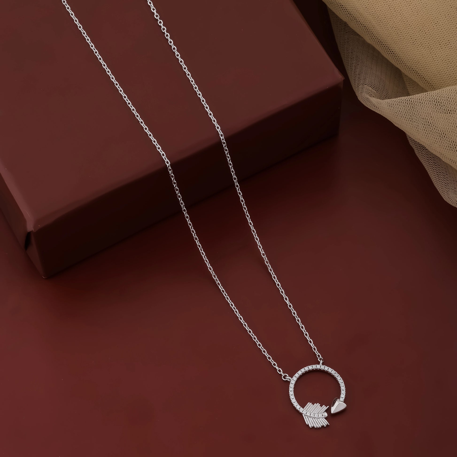 Silver necklace with a circular pendant on a dark red surface