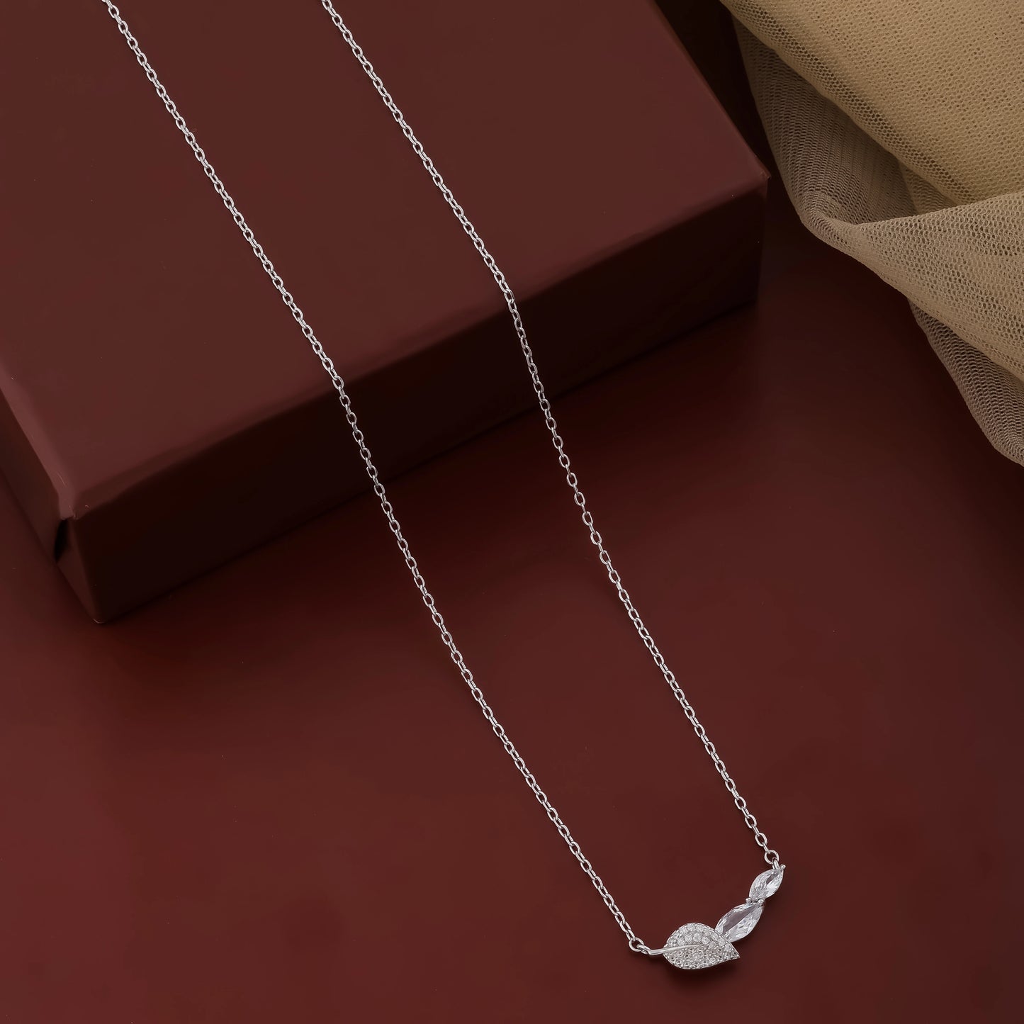 Silver necklace with a leaf pendant on a dark brown surface