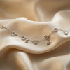 Silver anklet with heart and star charms on a beige fabric background