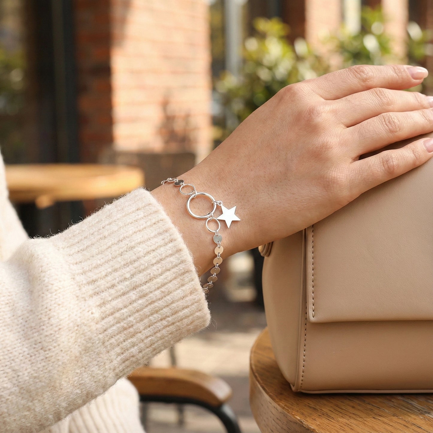Hand wearing a silver bracelet with star charm in an outdoor setting