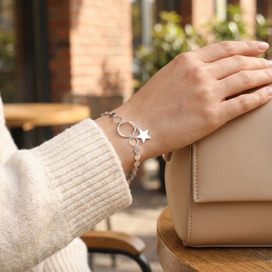 Hand wearing a silver bracelet with star charm in an outdoor setting