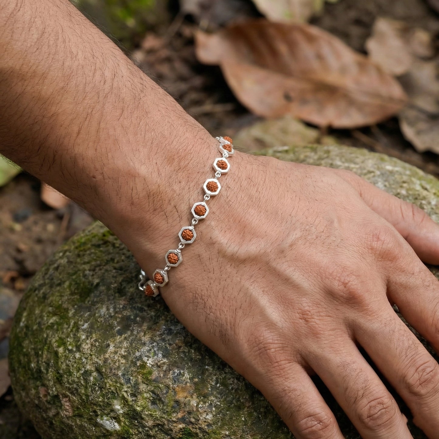 Hand wearing a silver bracelet with orange stones on a natural background