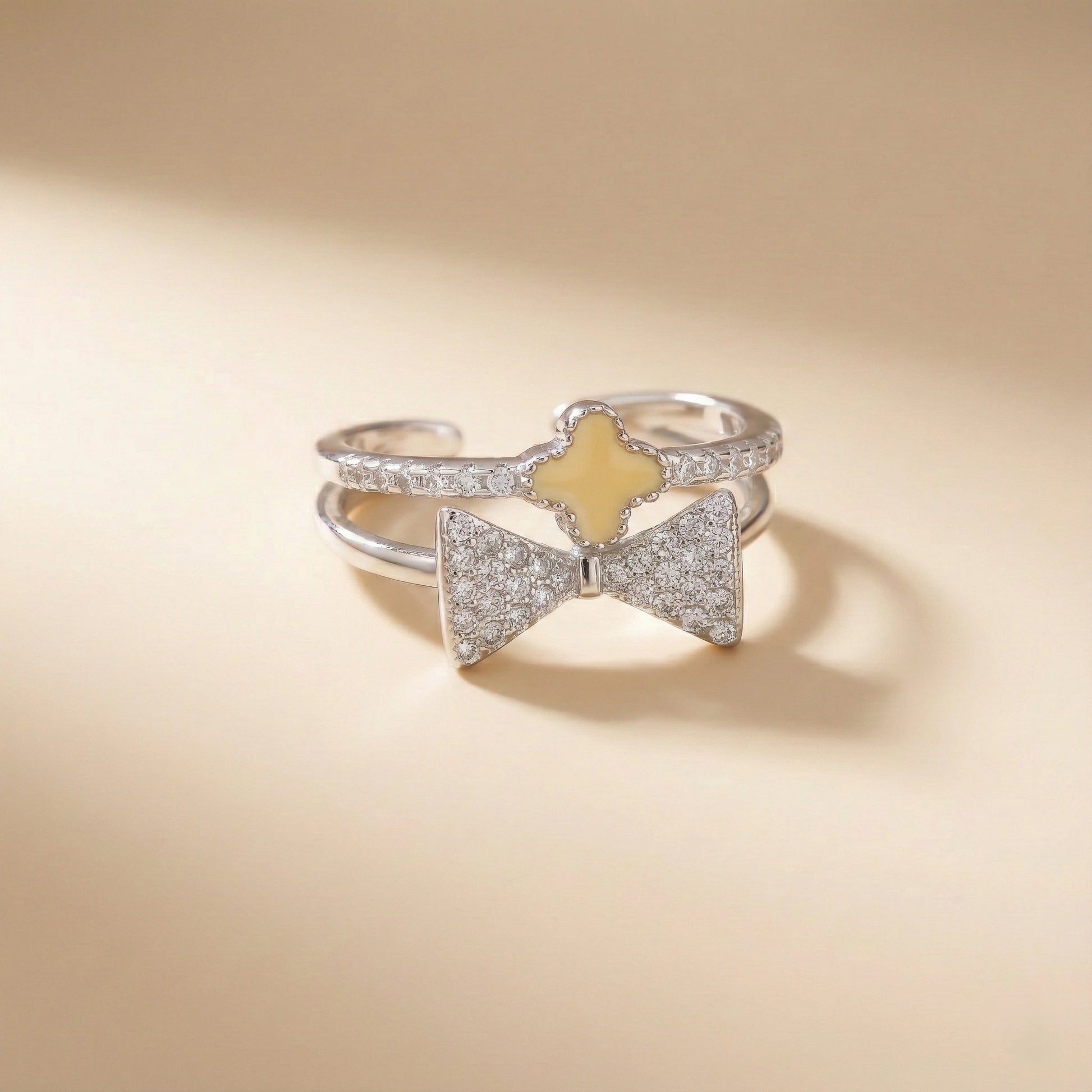Silver bow-shaped ring with a yellow center on a beige background