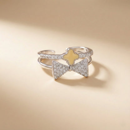 Silver bow-shaped ring with a yellow center on a beige background