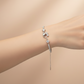 Silver bracelet with a heart and chain detail on a wrist against a beige background