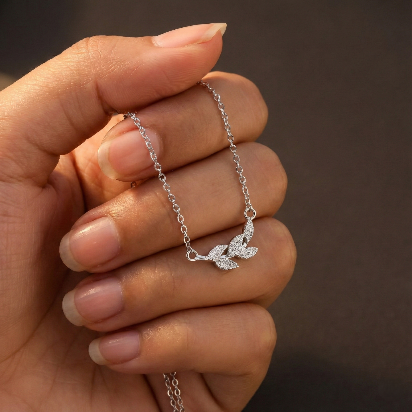 Silver leaf-shaped bracelet held by a hand against a brown background