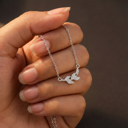 Silver leaf-shaped bracelet held by a hand against a brown background