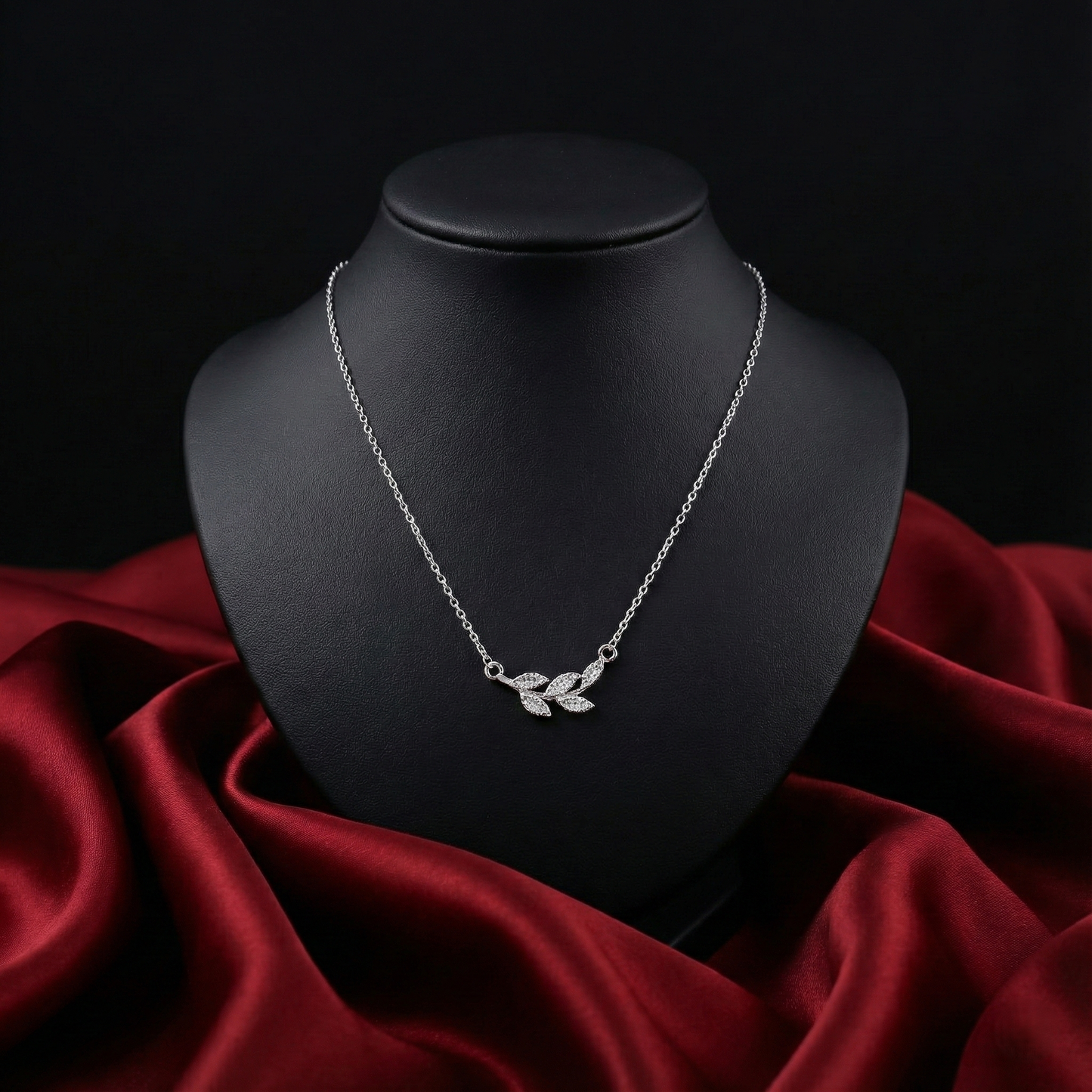 Silver necklace with leaf design on a black mannequin bust against a red fabric background