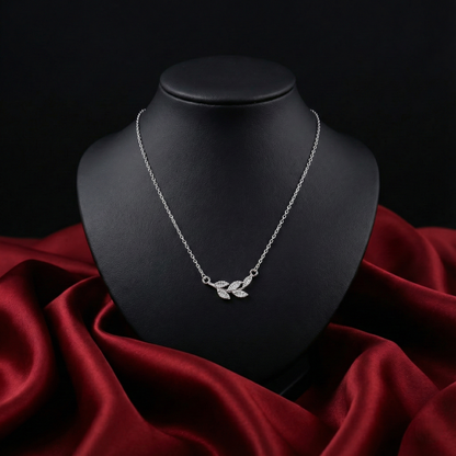 Silver necklace with leaf design on a black mannequin bust against a red fabric background